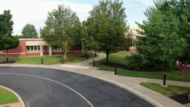 School bus point of view POV entering school building campus, new red brick school building aerial flying view