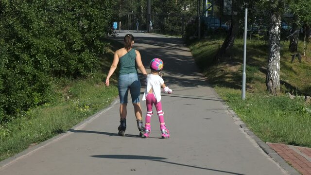 Little Girl with Mother Roller Skating Together Outdoors. Back Side View. Slow Motion. Summer Family Activities and Healthy Lifestyle Concept
