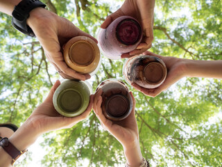 bottom view of people holding coffee cup and cheer in garden. Friends having coffee break outdoor together.