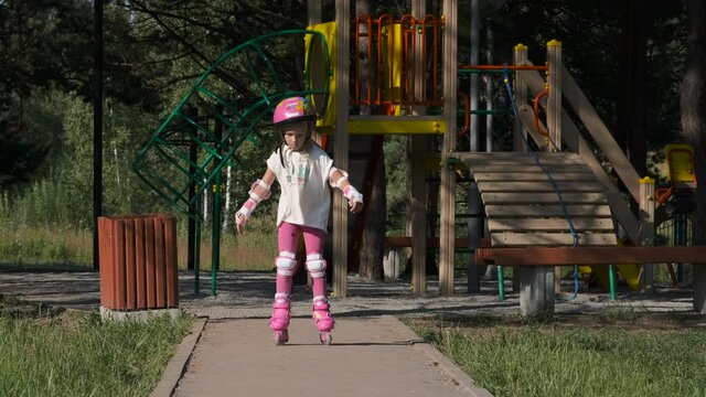 Little Girl in Helmet Learning to Roller Skate in a City Park. Slow Motion. Childhood, Summer Activities and Healthy Lifestyle Concept