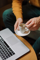 Cropped unrecognizable man drinking coffee and working on laptop in coffee shop.