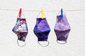 Drei bunt gemusterte Gesichtsmasken zum Trocknen auf Leine aufgehängt vor weißem Hintergrund