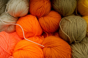 Balls of warm-colored yarn lie on store shelves for sale.