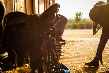 Equestrian tools stored in a stable at evening at the end of the eequestrian training  with sunset backlight and a girl walking on the backfground