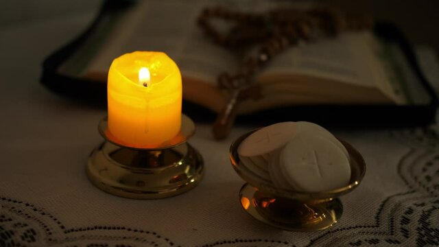 Communion hosts in twilight illuminated by the light of a lit candle rosary