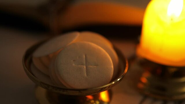 Communion hosts in twilight illuminated by the light of a lit candle