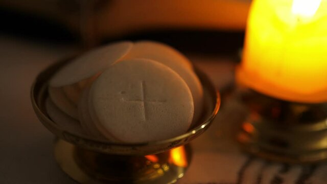 Communion hosts in twilight illuminated by the light of a lit candle