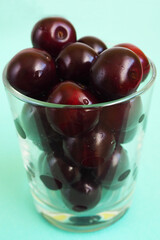 red juicy cherry in a clear glass glass on a blue background side view . ripe summer berries