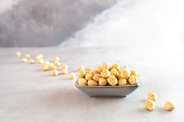 Golden peeled hazelnuts in a gray rectangular bowl stands on a gray concrete background. Raw peeled hazelnuts lie in one line. Raw food concept. Vegetarian food. Healthy food, snacks
