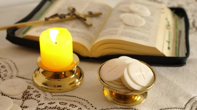 communion hosts lit candle and holy bible cross with jesus