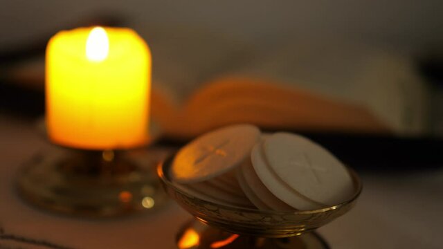 Communion hosts in twilight illuminated by the light of a lit candle