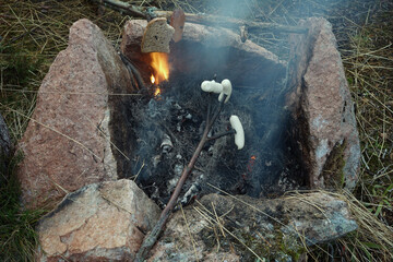 Sausages and bread on tree sticks above the campfire.