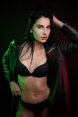 beautiful hot brunette girl posing in a photo Studio on a dark background d leather raincoat neon light