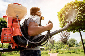 Gardener in protective mask and glasses spraying toxic pesticides trees