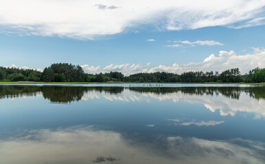 mirrored blue sky with white clouds and forest in a lake surface