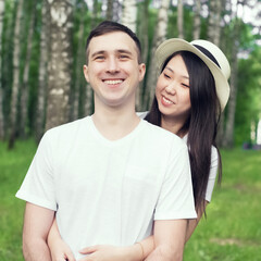 A happy young couple of asian woman and caucasian man is sharing smile and walking in countryside. Concept of mixed race couple in love. Female in hat is hugging her husband. Family. Love.