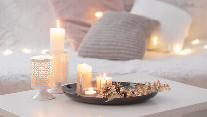 Christmas decoration   with burning candles on  white table against the background of  sofa with plaids and pillows. Cozy home and holiday concept