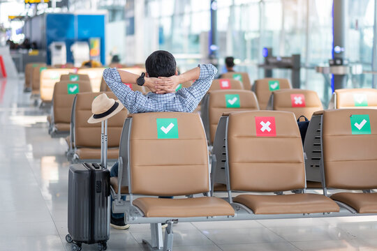 Young male wear face mask sitting on chair in airport terminal, protection Coronavirus disease (Covid-19) infection, Hipster man traveler ready to travel. New Normal and social distancing concepts