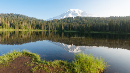 Mount Rainier, Washington mountain peak with a reflection in the water, surrounded by green trees.