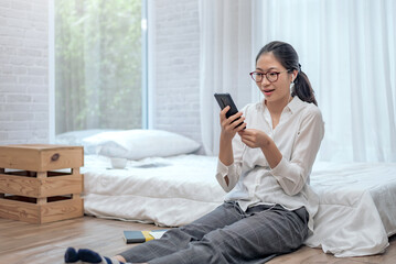 Young asian woman wears headphones to talk and video conferencing on mobile phone in the bedroom at home.