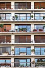 Obraz premium Balconies of a modern building with plants and shutters. City facade of apartment building with Windows, balconies and flowers