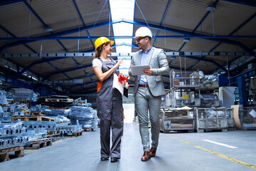 Manager supervisor and industrial worker in uniform walking in large metal factory hall and talking...