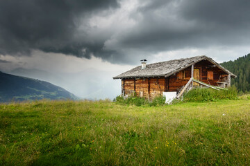 Fototapeta na wymiar Almhütte mit Schindeldach in den Alpen und Gewitterwolken im Hintergrund