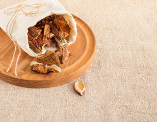 Dried mushrooms in a canvas bag scattered on a wooden tray on a background of burlap. Organic, eco-friendly food