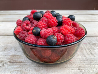 Ripe raspberries and blackcurrants in a glass vase on a wooden table. Harvest. Fresh summer berries.