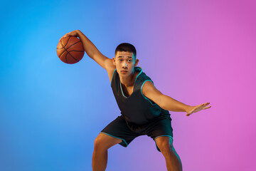 Winner. Young basketball player in action, motion on the run on gradient background in neon. Concept of sport, movement, energy and dynamic, healthy lifestyle. Training, practicing, trendy colors.