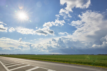 Asphalt highway with road markings on the background of blue sky and clouds.