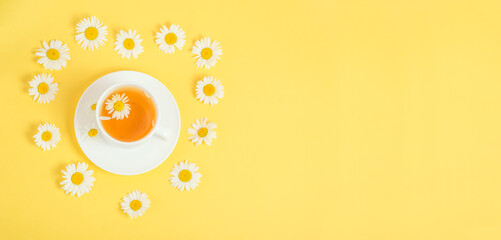 Chamomile tea on yellow background with copy space.