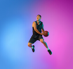 Fototapeta na wymiar Winner. Young basketball player in action, motion in high jump on gradient background in neon. Concept of sport, movement, energy and dynamic, healthy lifestyle. Training, practicing, trendy colors.