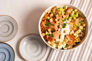 Ensalada Caesar con mucho pollo, salsa crotones de pan y maiz en un bowl blanco sobre un mantel de rayas con otros platos de ceramica en azules y beige para acompañantes.