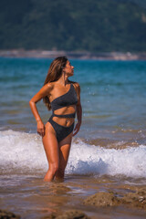 Lifestyle, Caucasian brunette in a luxurious black swimsuit with sparkles enjoying the summer at sea. Getting wet with the water of the waves