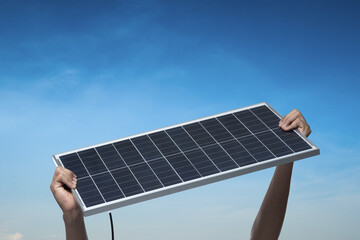 Hand holding a solar panel on blue sky background,alternative clean green energy concept