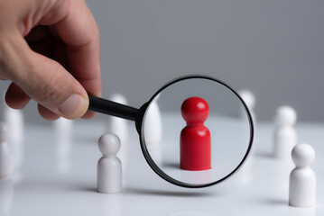 Person Hand Holding a magnifying glass looking to red wood people,Select a person in the team,...