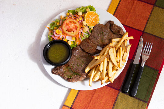Plato de comida con carne de res ensalada y papas a la francesa. Almuerzo tradicional en Latinoamerica de carne con papas y chimichurri