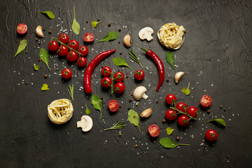 Pattern made up of cherry tomatoes, red pepper, garlic, mushrooms, pasta, arugula leaves and spices on a black background.