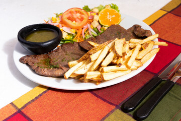 Plato de comida con carne de res ensalada y papas a la francesa. Almuerzo tradicional en Latinoamerica de carne con papas y chimichurri