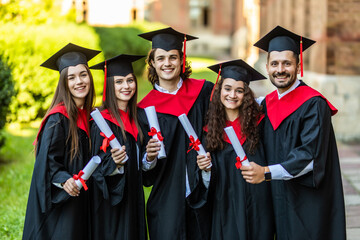 Five graduates posing in front of the university