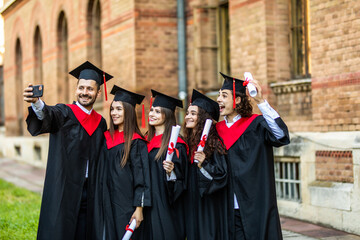 Capturing a happy moment. Four college graduates in graduation gowns standing close to each other and making selfie