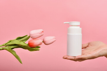 Natural skincare bottle, Hand showing cosmetic containers packaging with tulip flower essence extract, Organic beauty product concept.