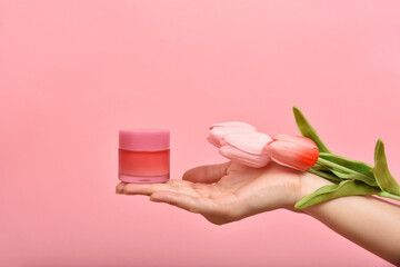 Natural skincare pink bottle, Hand showing cosmetic containers packaging with tulip flower essence extract, Organic beauty product concept.