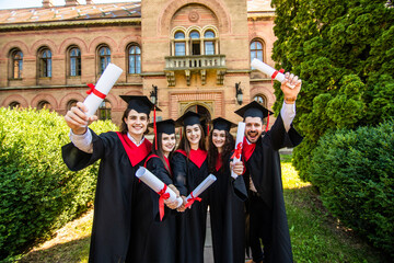 Happy graduation day. 5 graduates hold his graduate diplomas in their hands at University