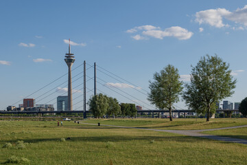 Fototapeta na wymiar Outdoor sunny scenery of natural promenade and green field on riverside of Rhine River, and background of skyline cityscape of Düsseldorf city and Rhine Tower, Germany in summer season.