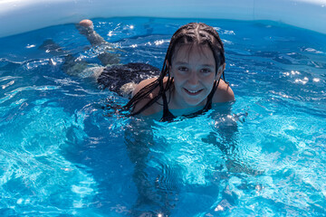 A cheerful girl with pigtails swims in an inflatable pool. Concepts of relaxation and rest