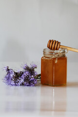 Glass jar filled with honey. Wooden spoon for honey. Natural product. Sweet food. Phacelia flower on a gray background. Blue, wildflowers. Side view.