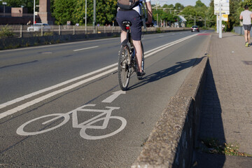 Fototapeta na wymiar Selected focus view at white bicycle icon symbol and people ride bicycle on bicycle lane beside road on the bridge cross Rhine River in Düsseldorf, Germany. Cycling friendly city concept in Europe. 