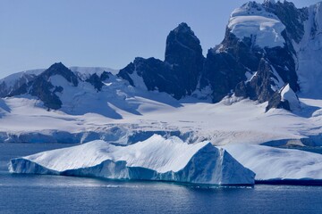 Fototapeta na wymiar Blue Iceberg in antarctic landscape, with mountains on a sunny day, Antarctica